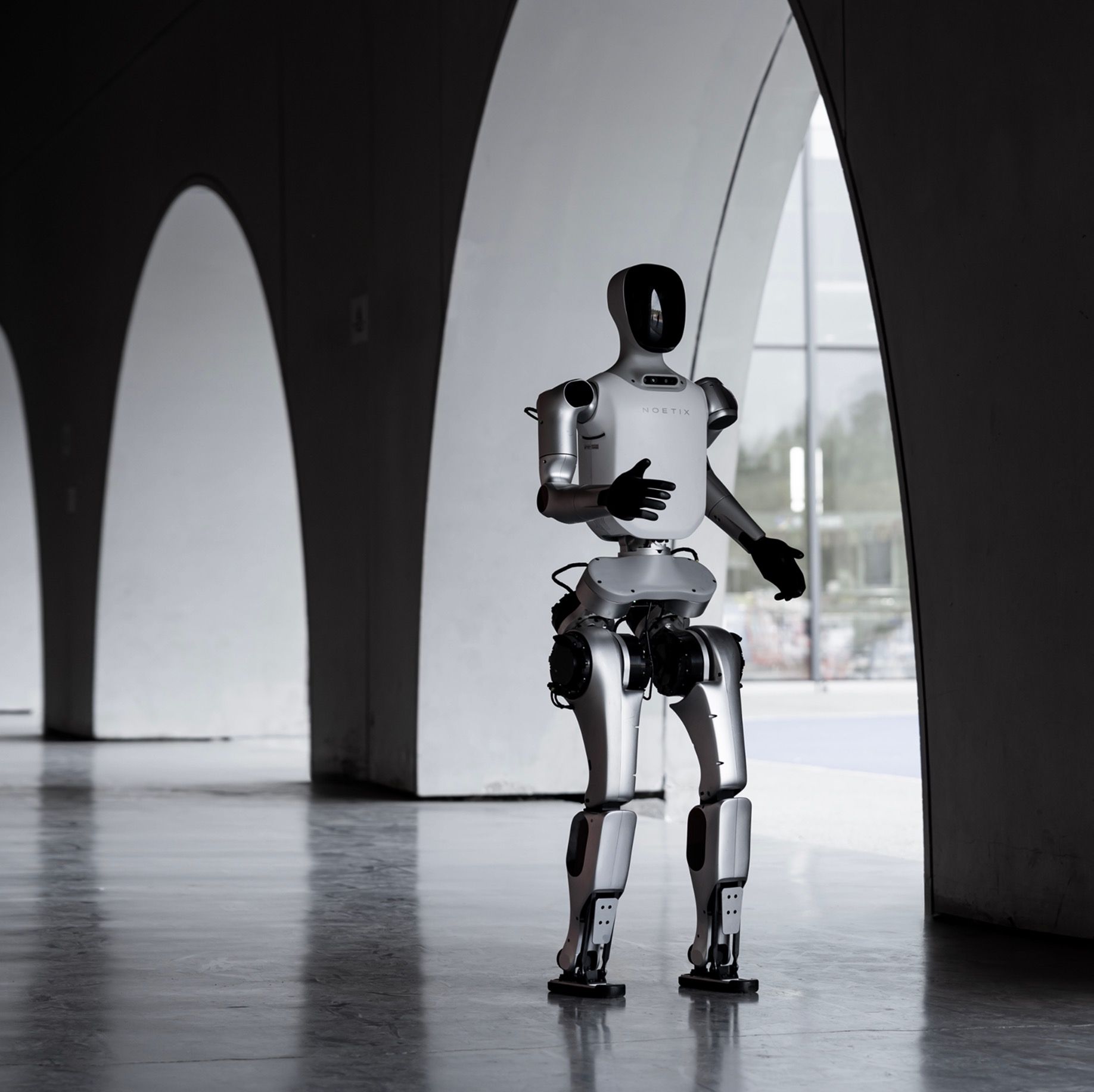 Noetix Robotics E1 humanoid robot standing in an arched hall, front three-quarter view, vendor product photo